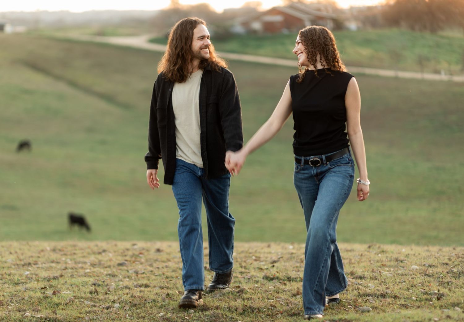 A couple strolls together across rolling green hills during golden hour.
