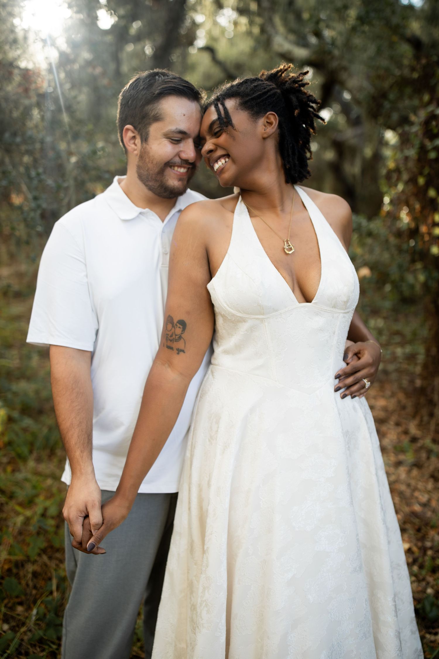 A tender moment captured between a couple in white attire against a natural outdoor setting.