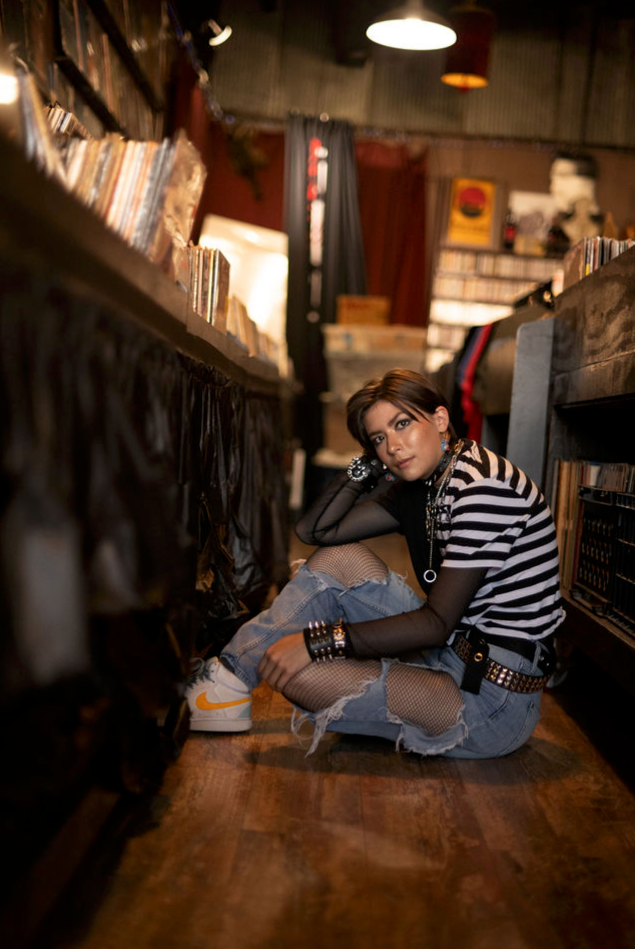 Young person in plaid shirt and jeans sits casually on concrete steps in outdoor portrait series.