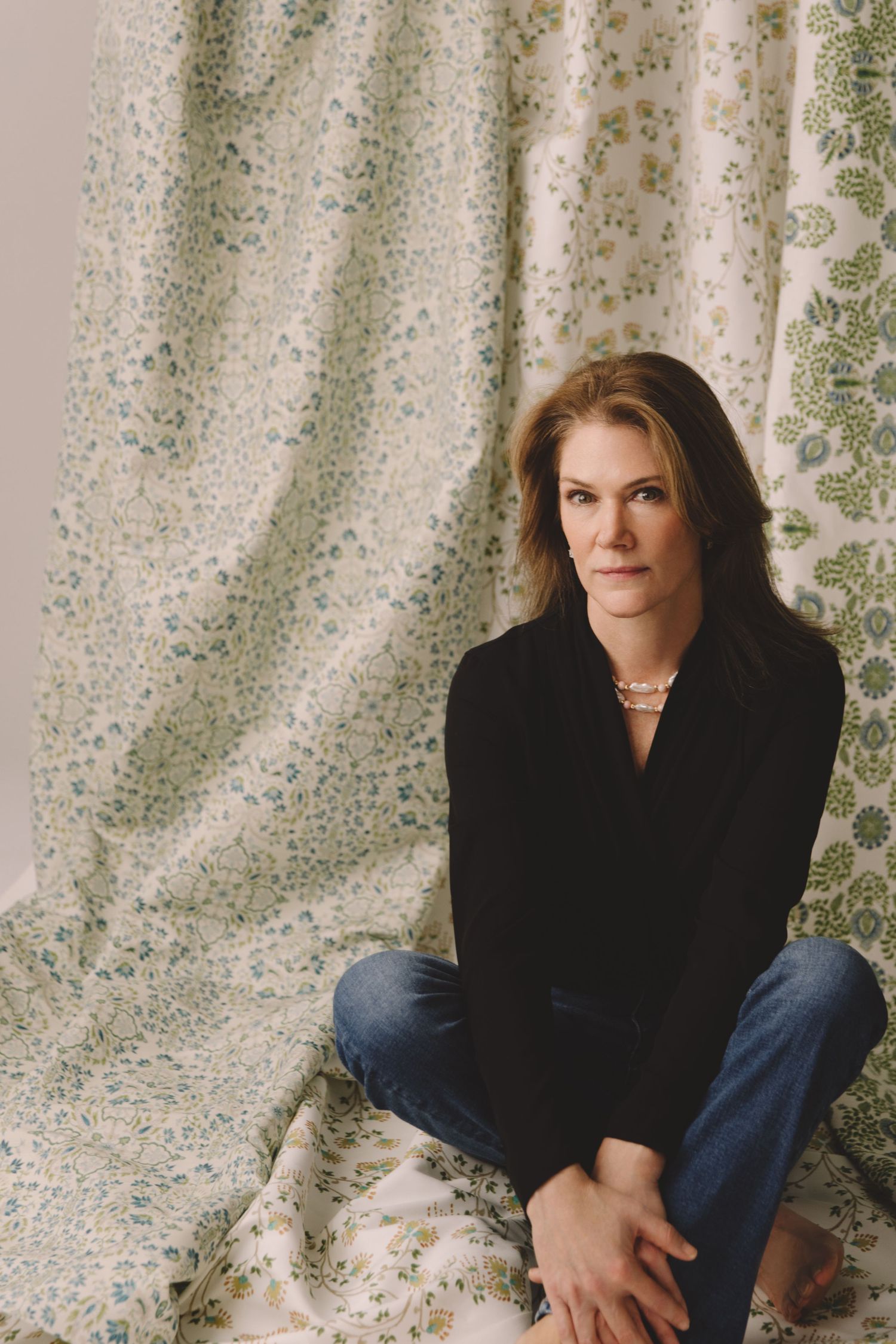 A person in a black sweater and jeans sits casually against a textured white backdrop in a series of candid poses.