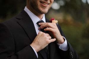 Close-up shot of someone adjusting a black tie against a formal suit jacket.