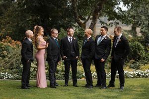 Wedding party members in formal attire stand together on a grassy lawn during an outdoor celebration.