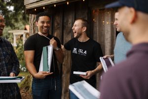 Groomsmen share drinks and laughter during outdoor wedding celebration.