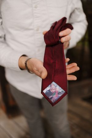 A burgundy necktie being unfolded to reveal a hidden photograph tucked inside the fabric.
