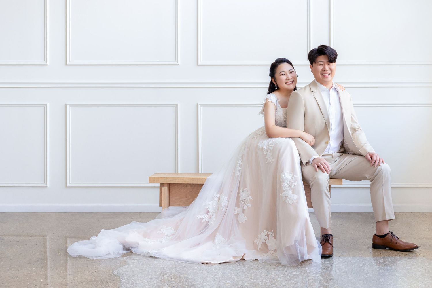 A couple in wedding attire poses elegantly against a white wall in a romantic photoshoot series.
