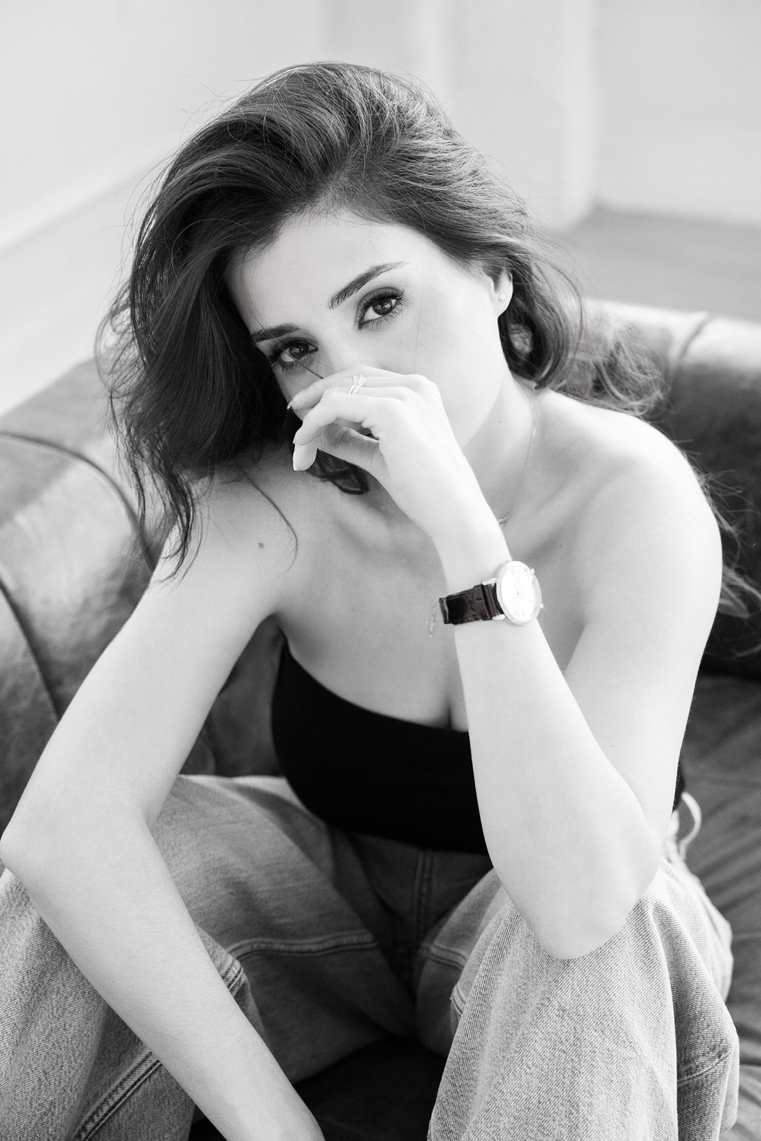 Artistic black and white portrait of a woman in a black top resting on a couch with a thoughtful expression.