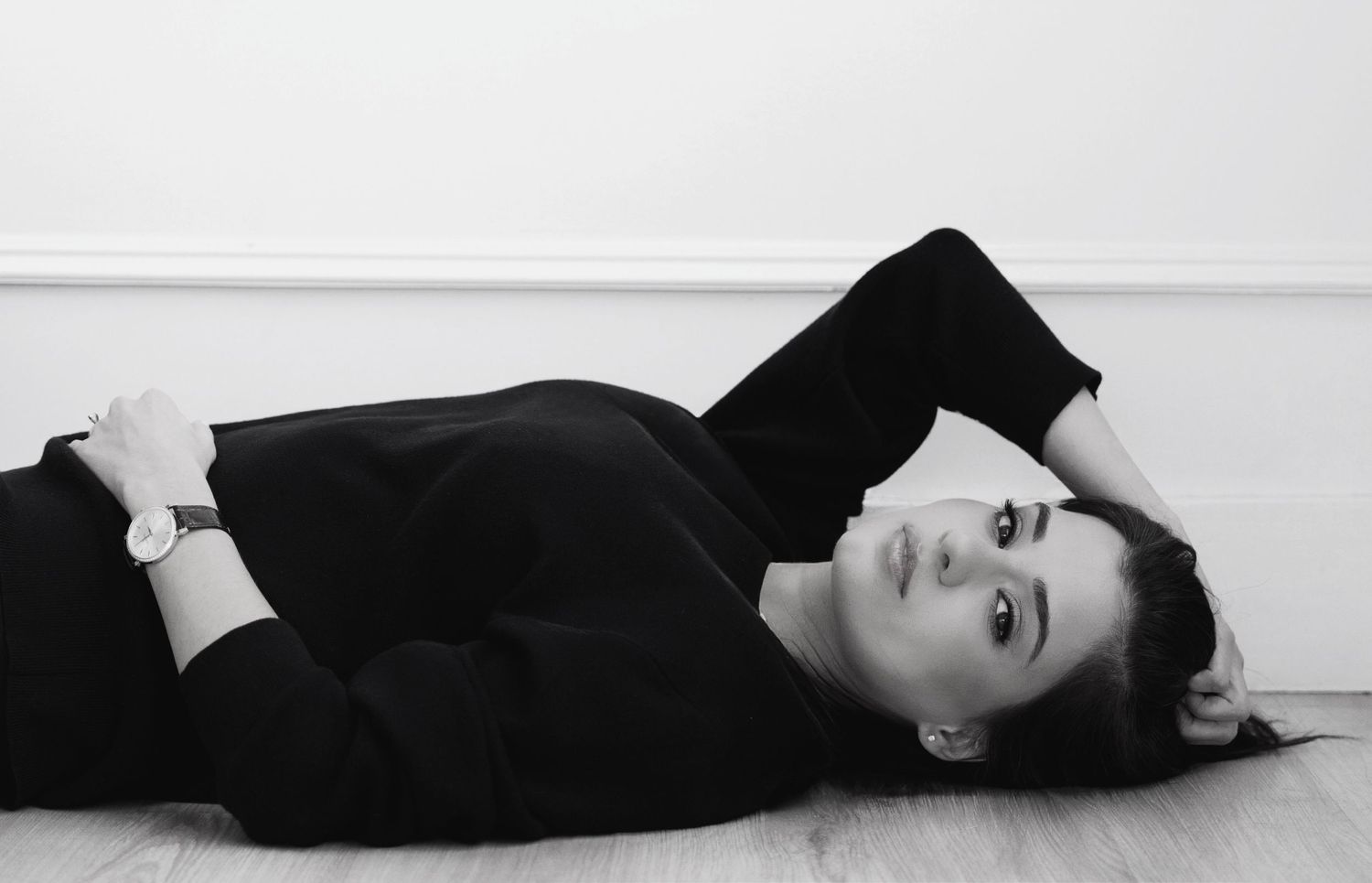 Dramatic black and white photo of a woman lying down in dark clothing against a light background.