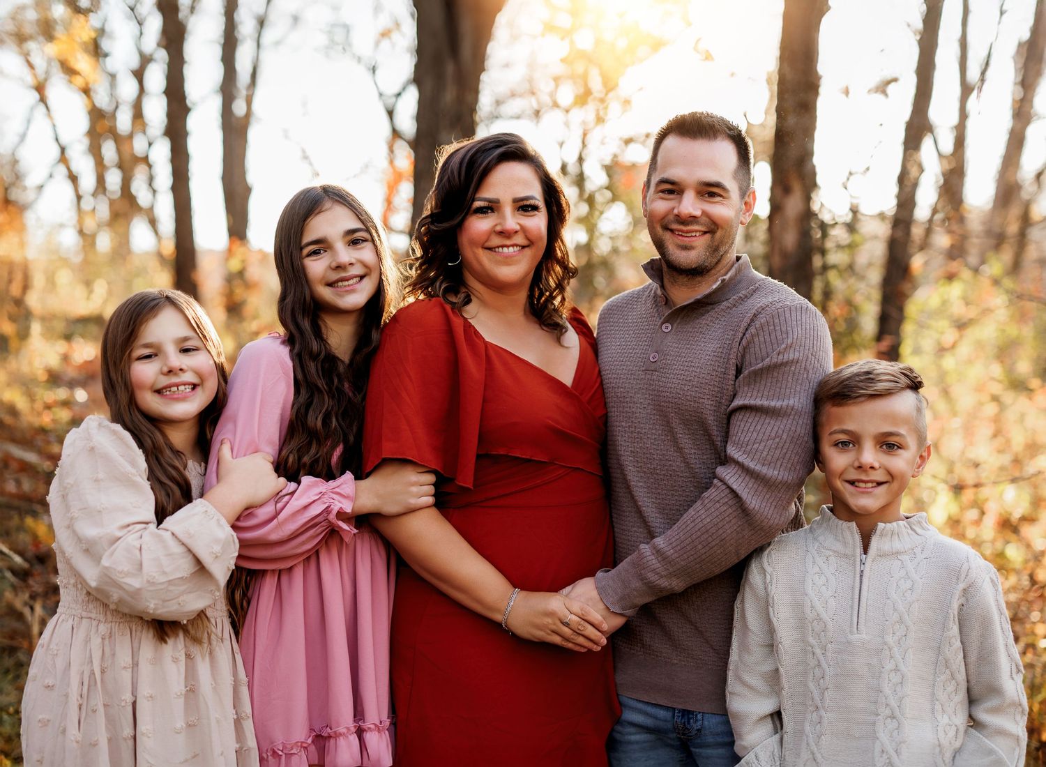 A group poses together in autumn woods wearing coordinated red and neutral colored outfits for a family photo session.