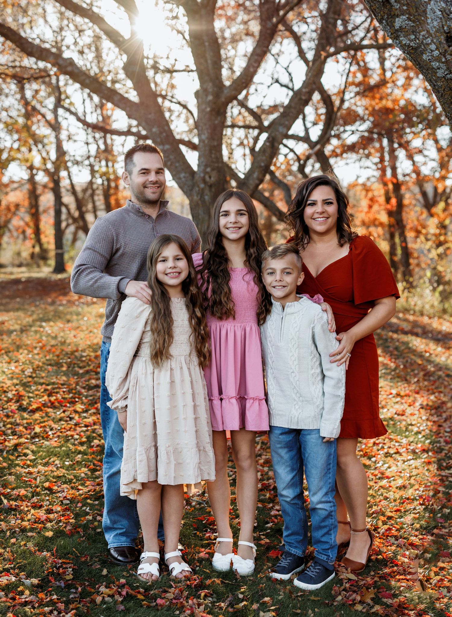 A group poses together in a forest setting with vibrant autumn foliage and fallen leaves on the ground.
