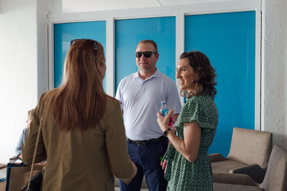 Three professionals networking at an indoor corporate event with bright blue wall panels in background.