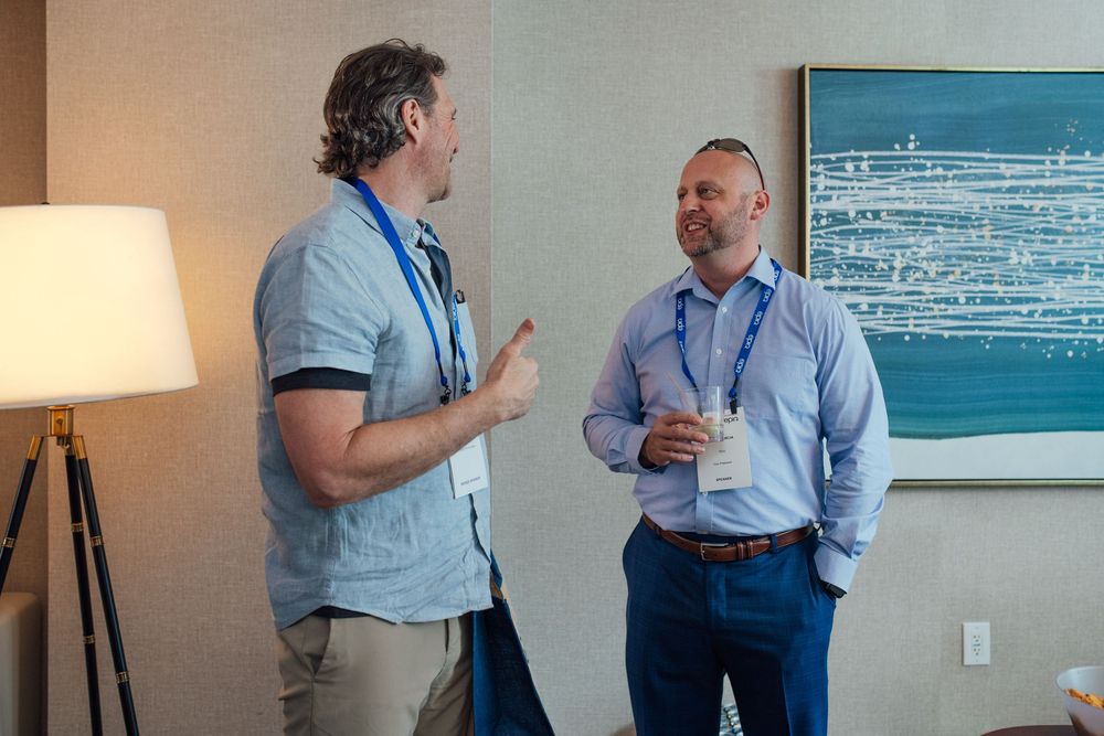 Two business professionals with lanyards having a conversation at an indoor corporate networking event.