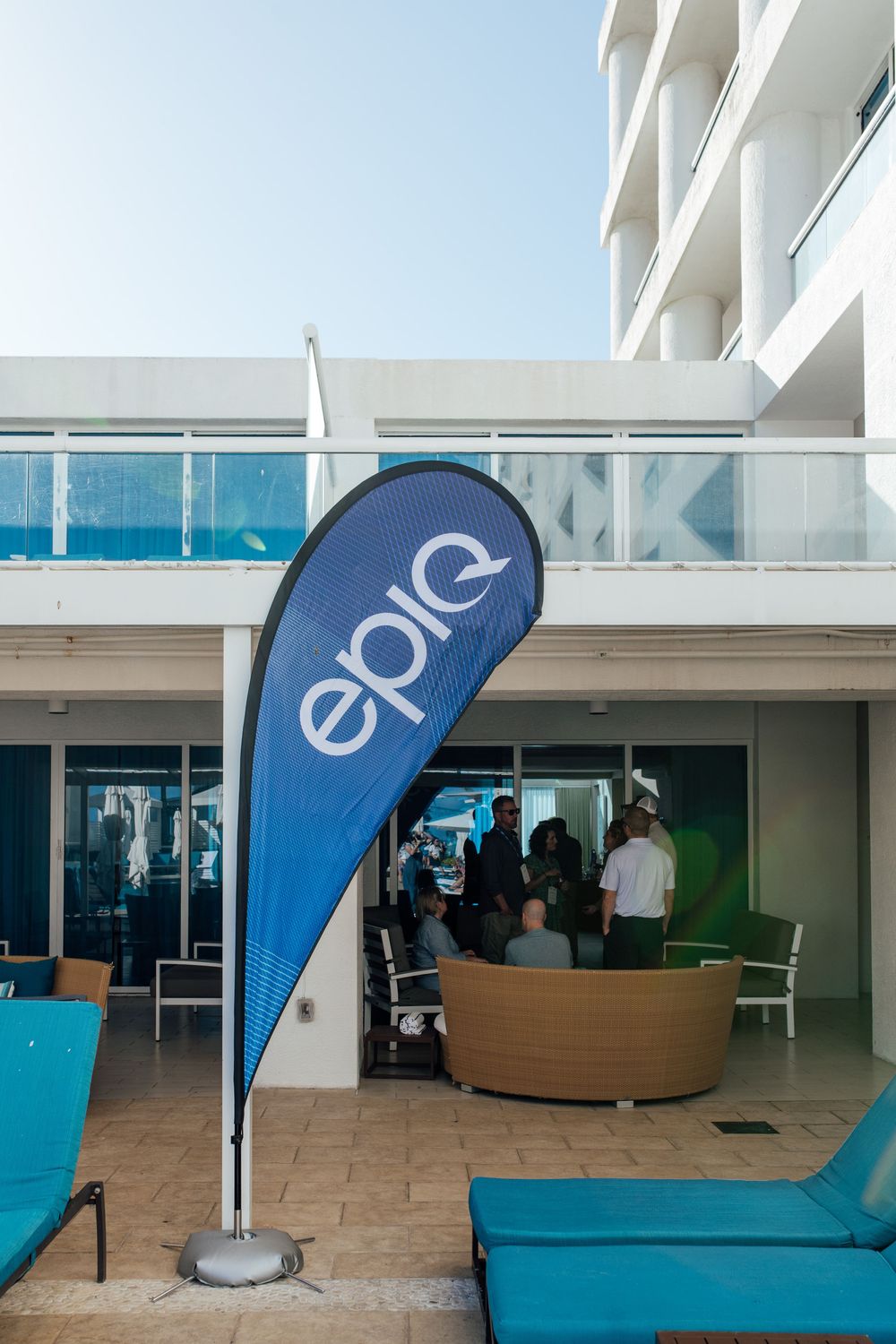 Epiq company branded teardrop flag at outdoor hotel event space with guests networking near poolside cabana.