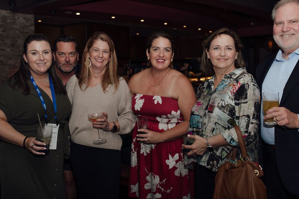 Group of six professionals smiling and socializing at a casual corporate networking event.