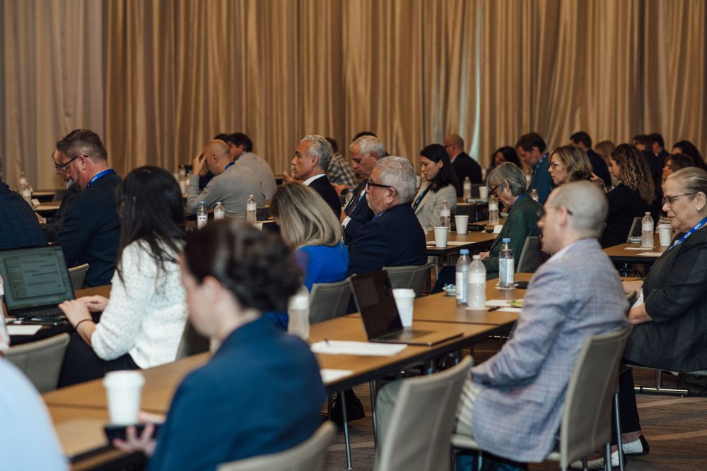 Large group of business professionals seated at tables during a corporate conference session.