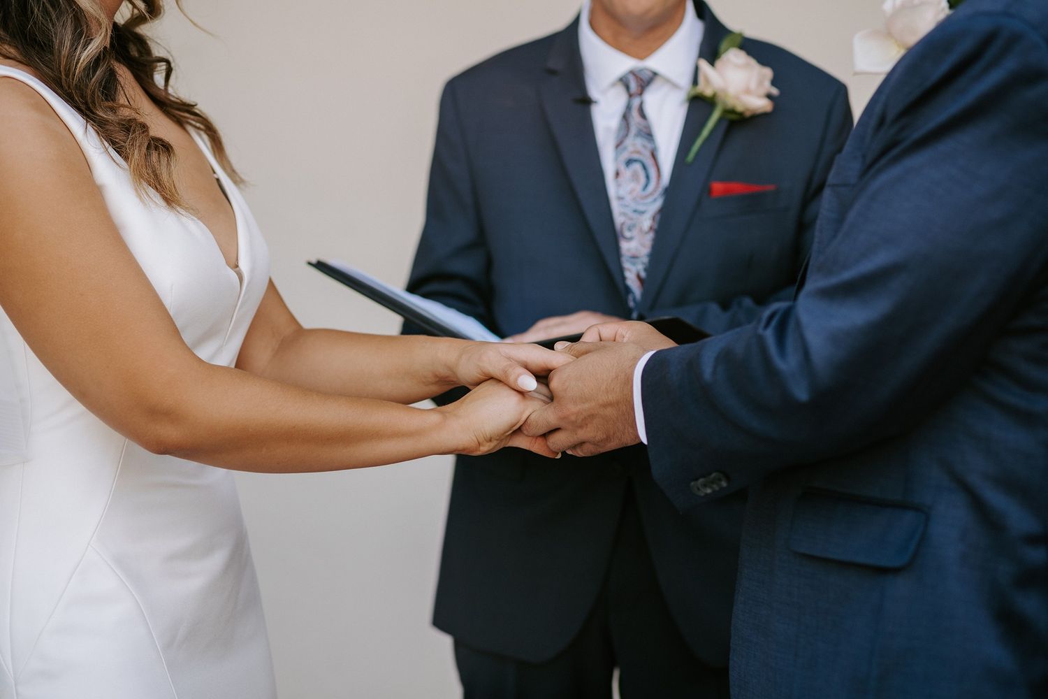 Bride and groom holding hands during wedding ceremony with officiant holding book in background at Darlington House.