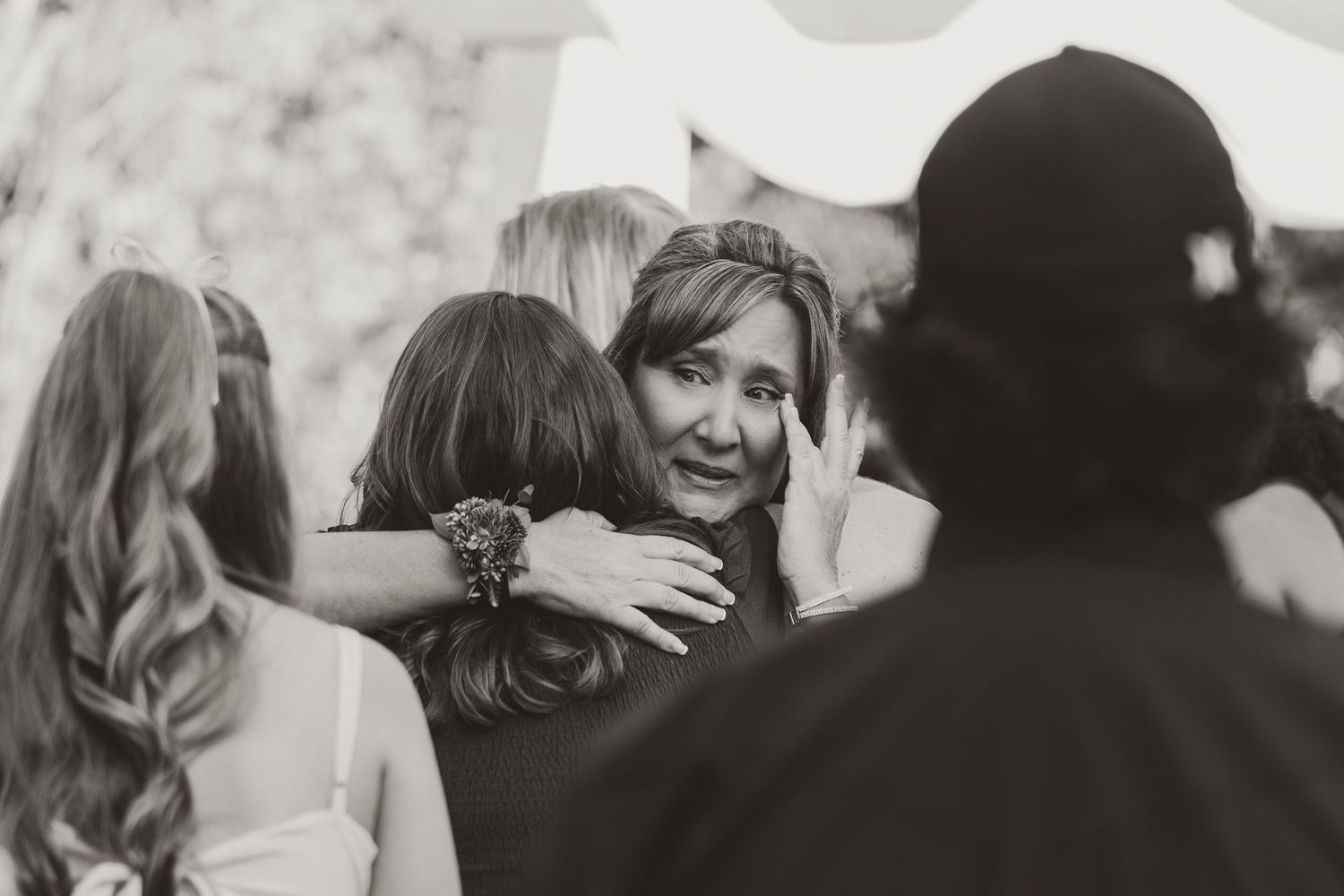 Emotional black and white photo of woman tearfully embracing bride at outdoor wedding.
