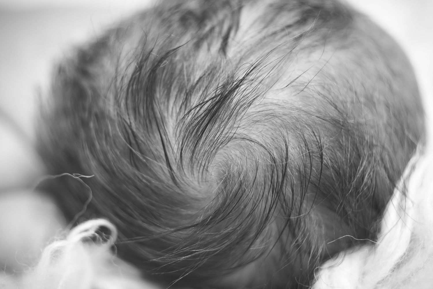 Close-up black and white photo of a newborn baby's head showing a natural hair whorl pattern.