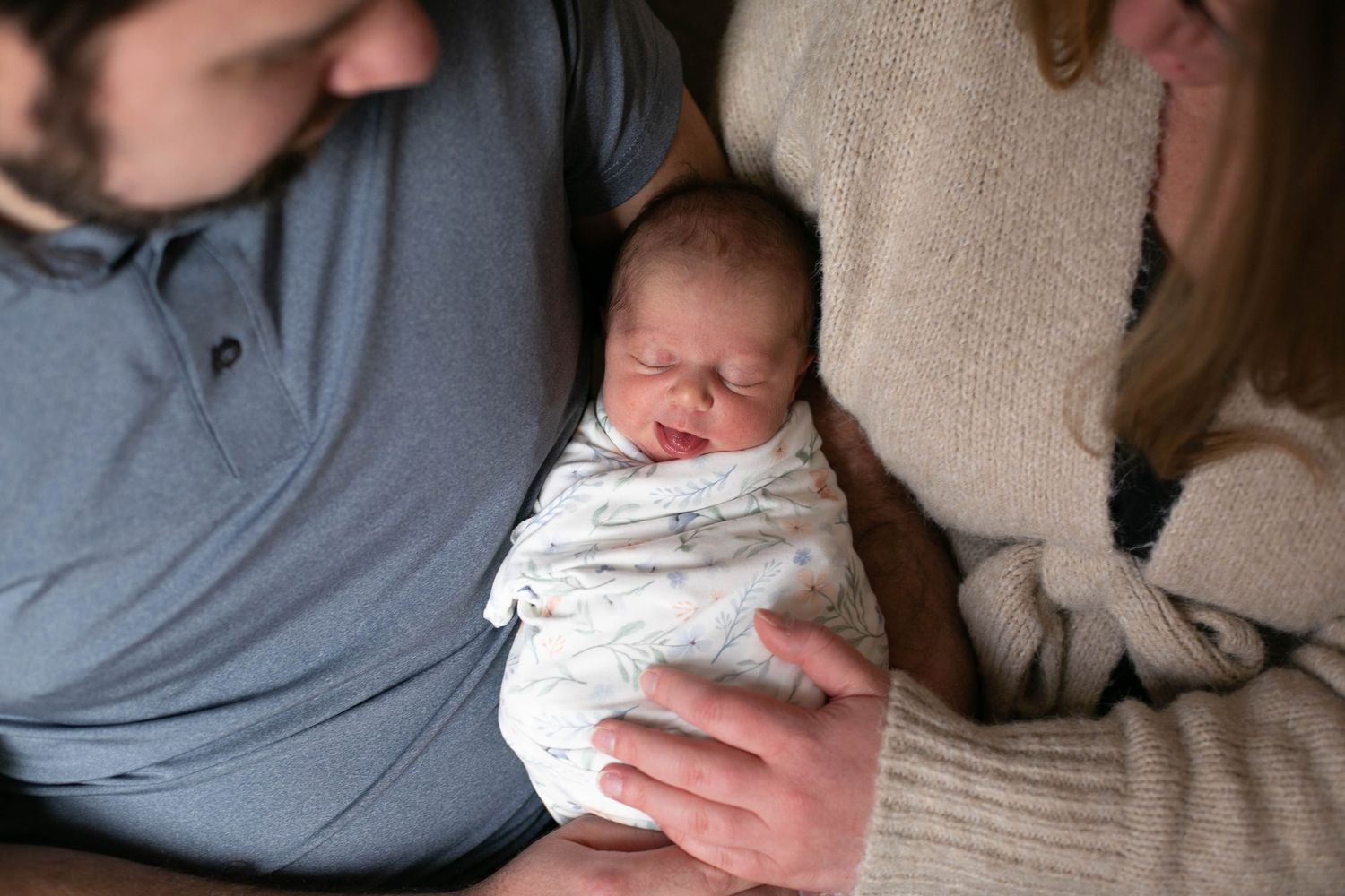 Parents cradling their swaddled newborn baby, a tender family moment captured in warm, natural light.