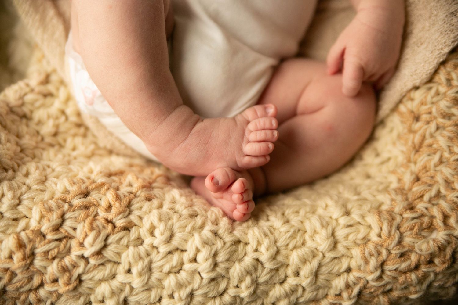 Close-up of a newborn baby's tiny feet and hands resting on a soft cream knitted blanket.