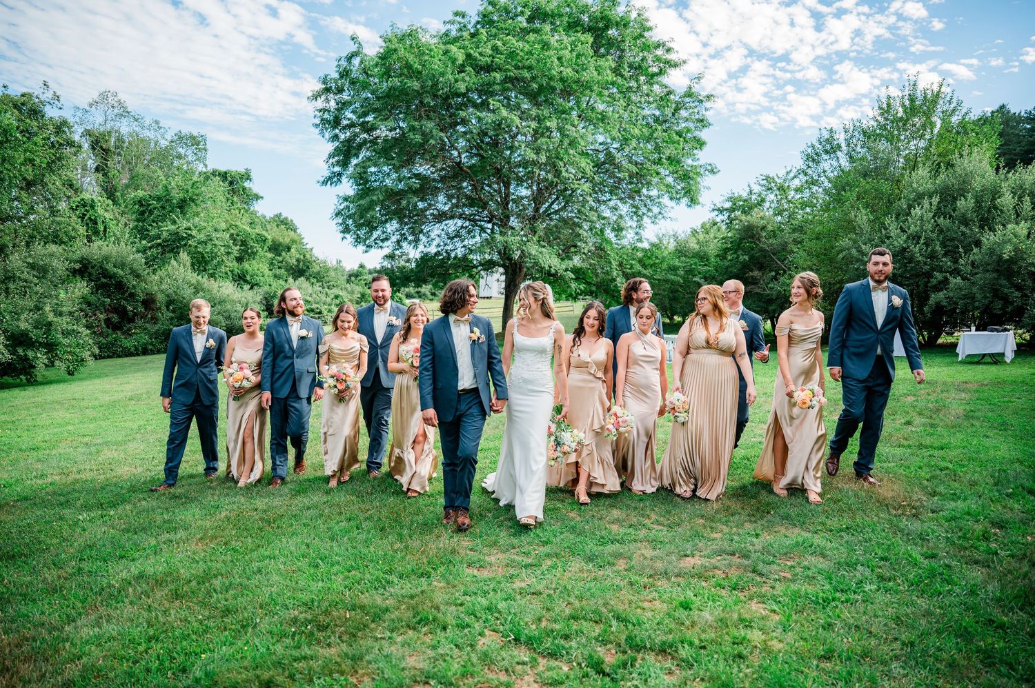 Wedding party poses together on a lush green hillside during an outdoor summer celebration.
