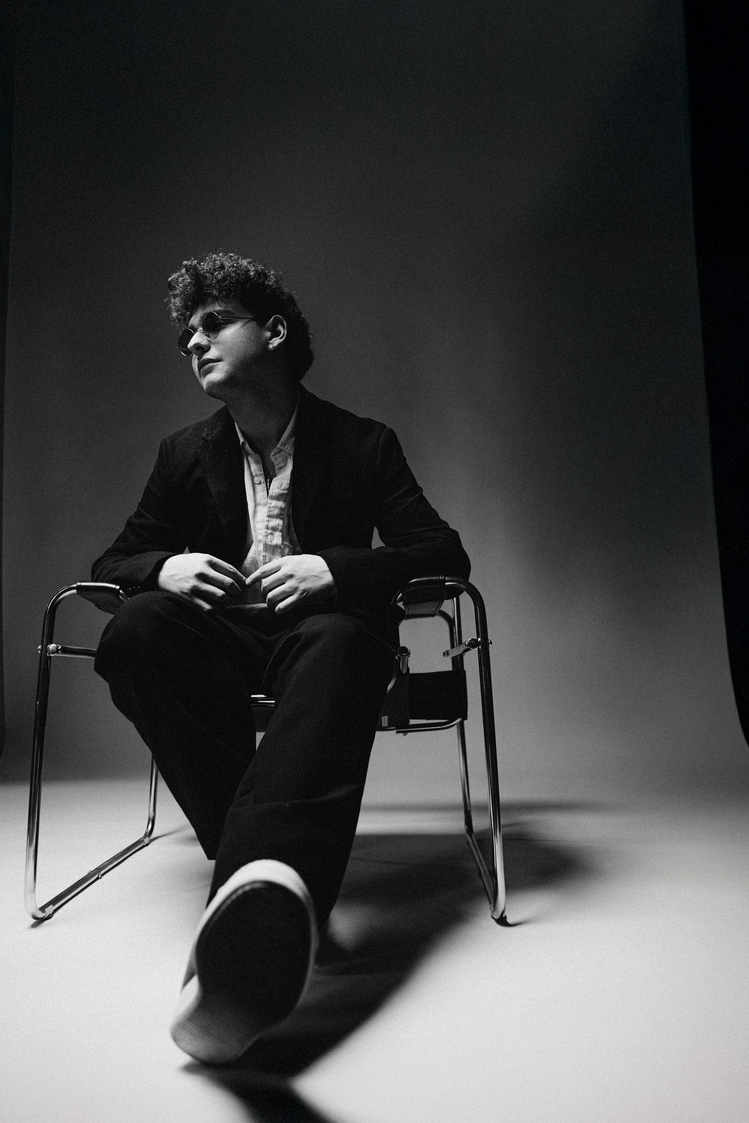 A dramatic black and white photo series shows a figure in dark clothing sitting in various poses on a chair against a stark background.