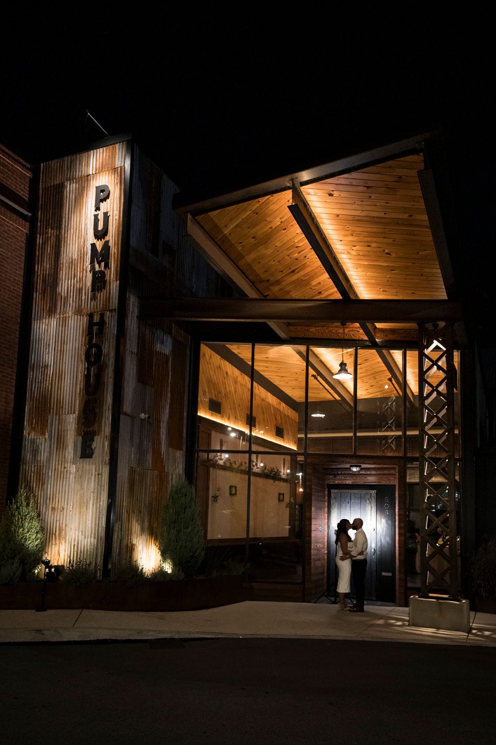 Exterior night view of a modern rustic barn venue with dramatic lighting and wooden architecture.