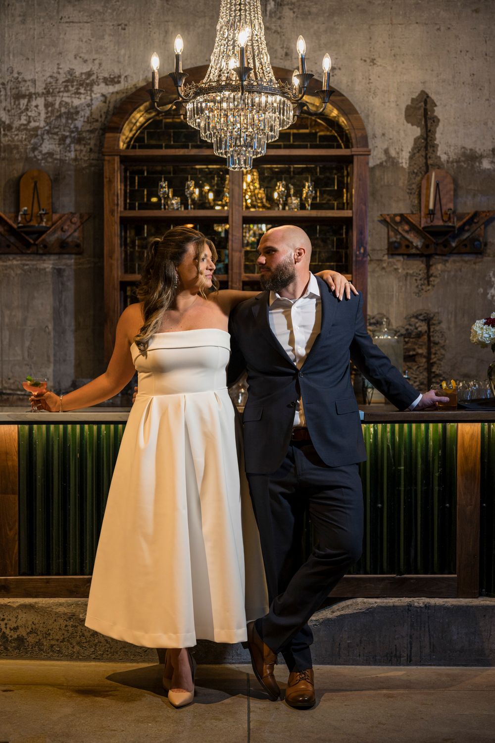 A couple sits together at an elegant bar with crystal chandeliers and vintage decor in a romantic setting.