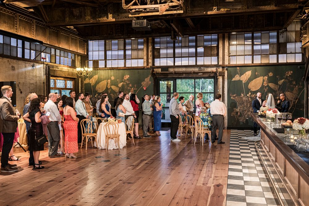 Wedding reception venue features checkered dance floor and large industrial windows with natural light.