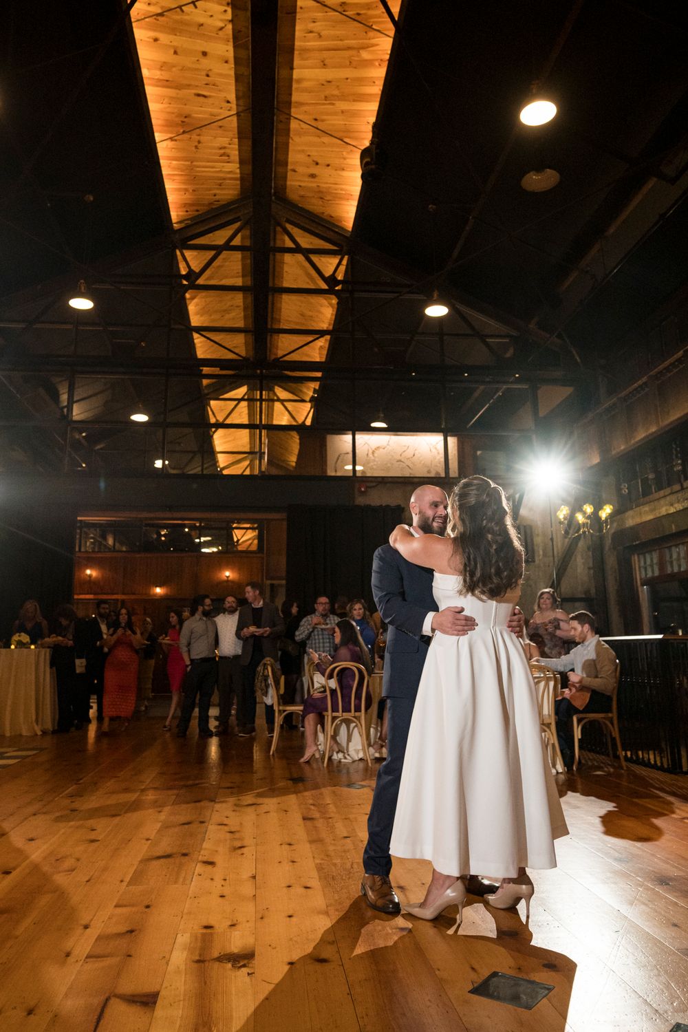 People dancing together in a rustic wooden venue with warm lighting and hardwood floors during a celebration event.