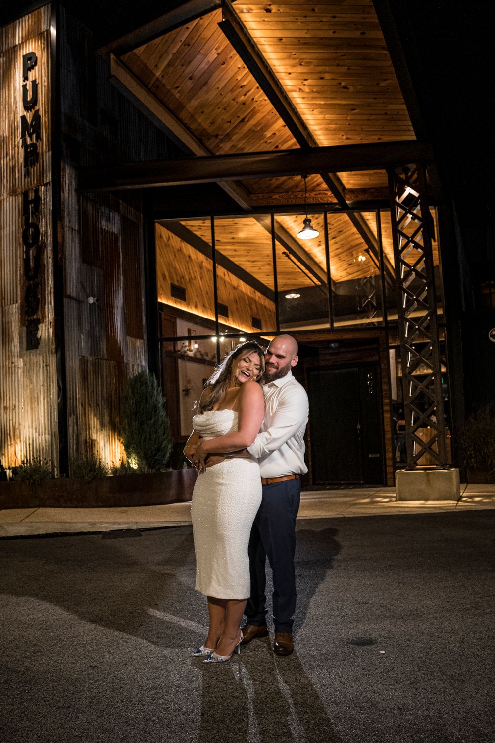 A couple shares a romantic dance together under warm wooden beams in a rustic barn venue at night.
