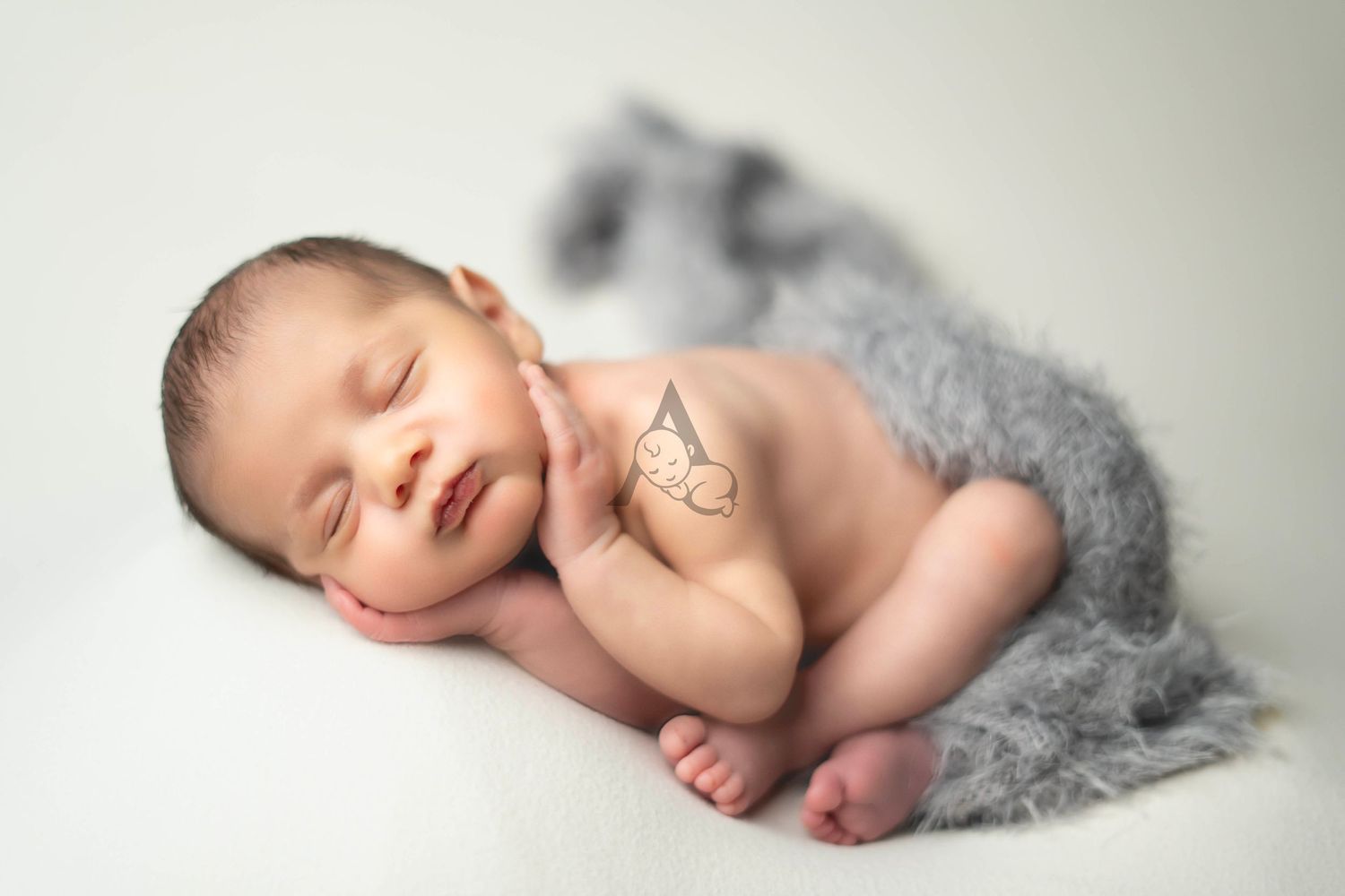 Peaceful sleeping newborn baby curled up on soft gray blanket against white background.
