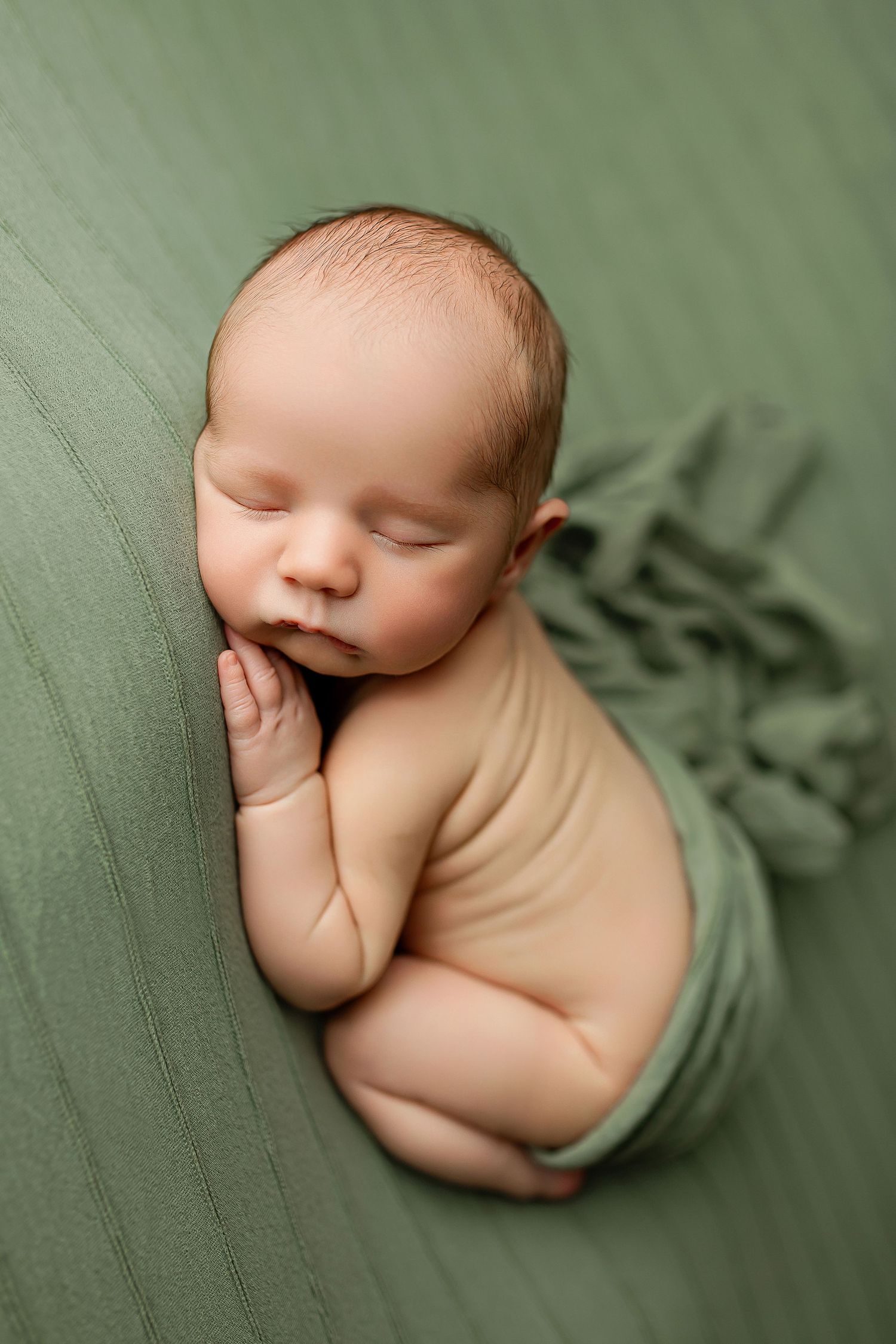 Newborn baby sleeping on sage green blanket during studio photography session