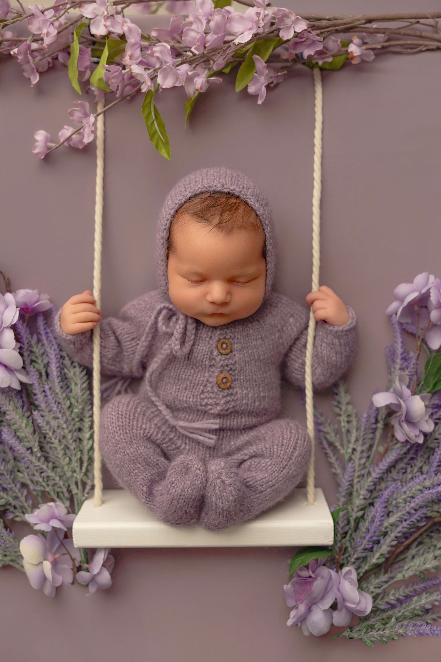 Two sleeping newborns nestled together in a rustic wooden basket with lace bedding and delicate floral decorations.