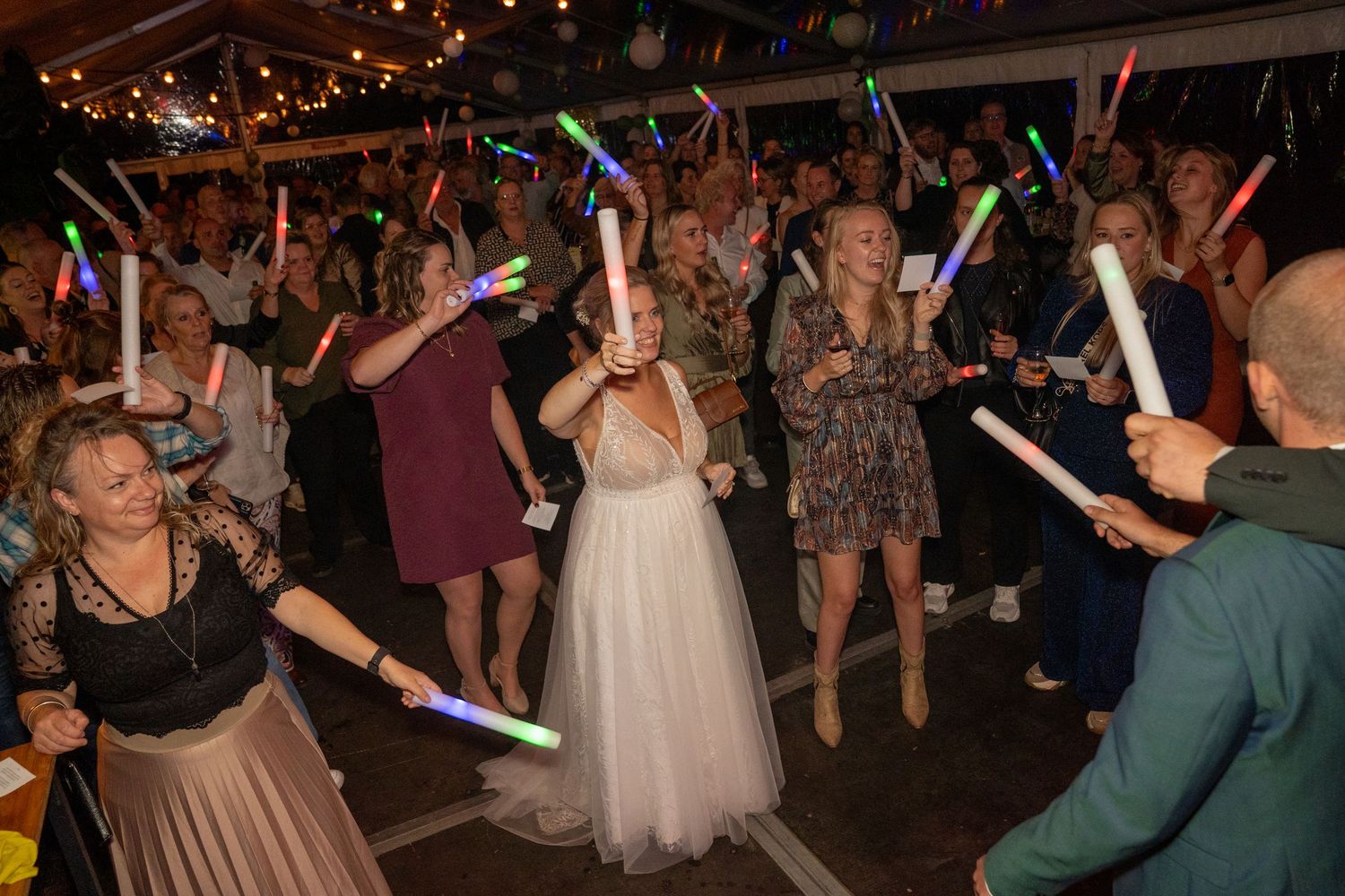 Bruid en gasten zwaaien met lichtgevende led-sticks op een volle dansvloer tijdens een bruiloftsreceptie. trouwfotograaf whijhe Olst leshof