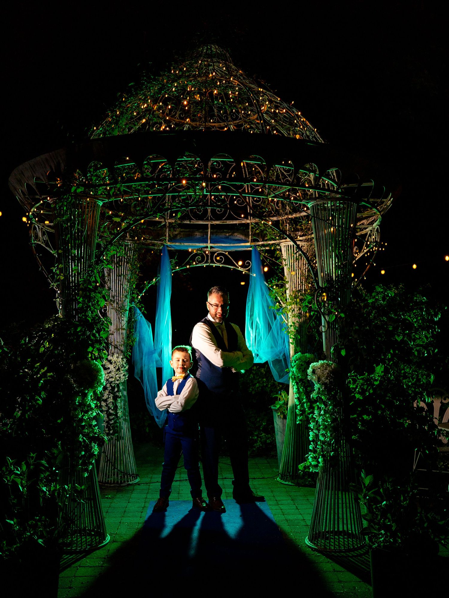 Couple posing under an illuminated gazebo with green and blue lights at a night wedding reception.