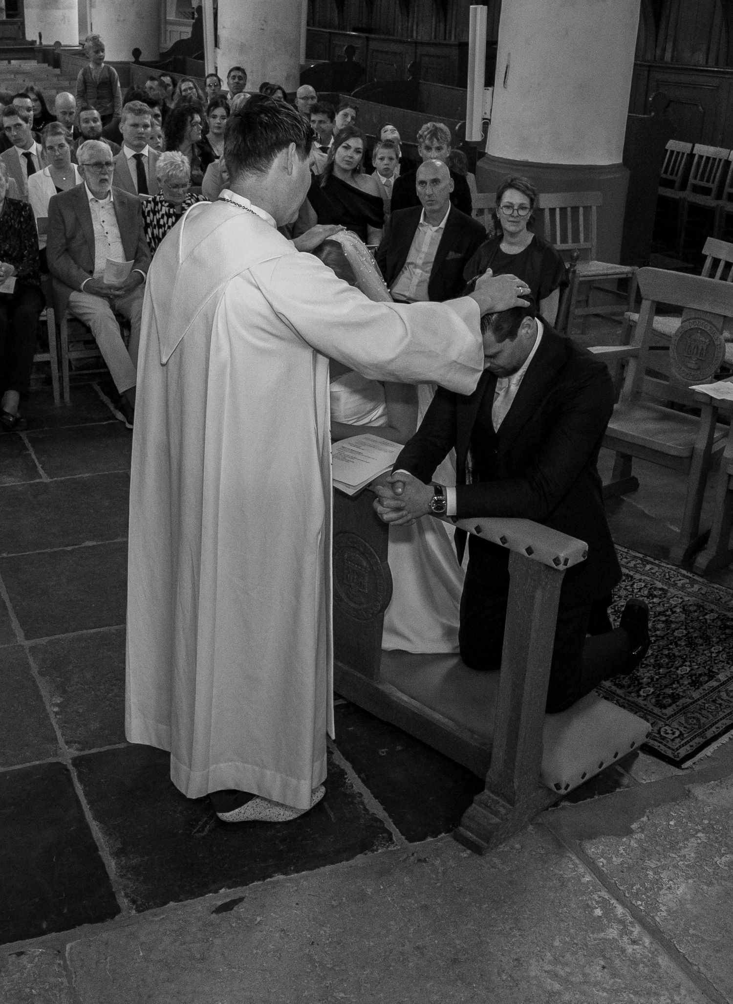 Zwart-witfoto van een priester die de knielende bruidegom zegent tijdens een traditionele kerkelijke huwelijksceremonie. christelijk