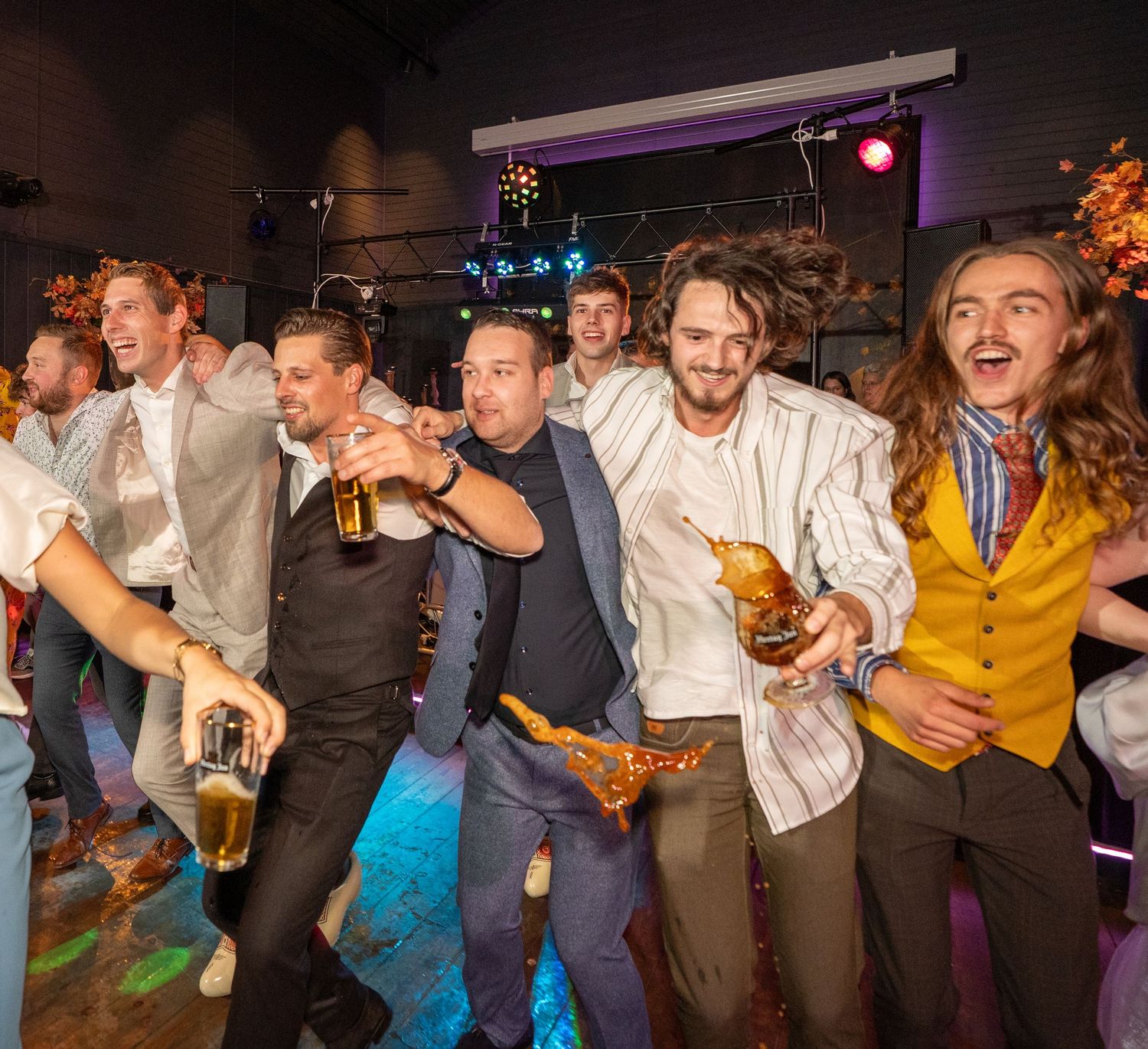Een groep mannen in pakken viert uitbundig feest op een dansvloer met kleurrijke verlichting. avondfeest trouwfotograaf Heerde