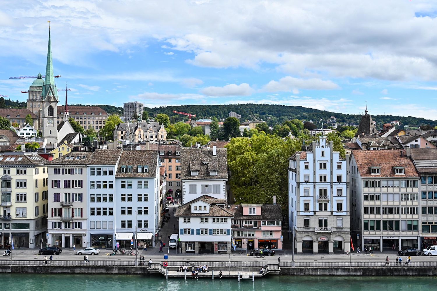 Panoramic cityscape view of historic buildings and architecture along a waterfront with mountains in the background.