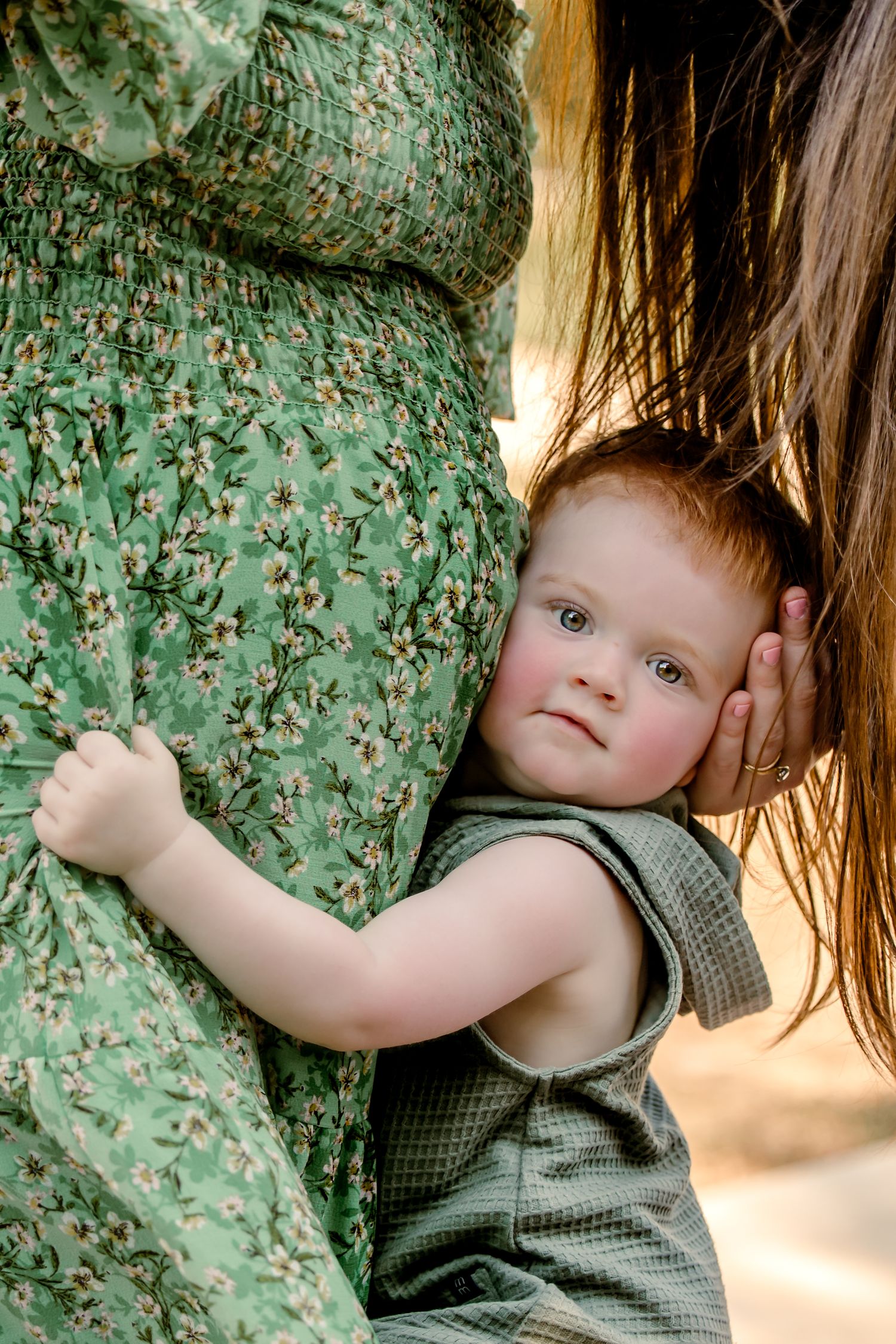 A baby in a green romper leans against a pregnant woman in green dress in DFW, TX.