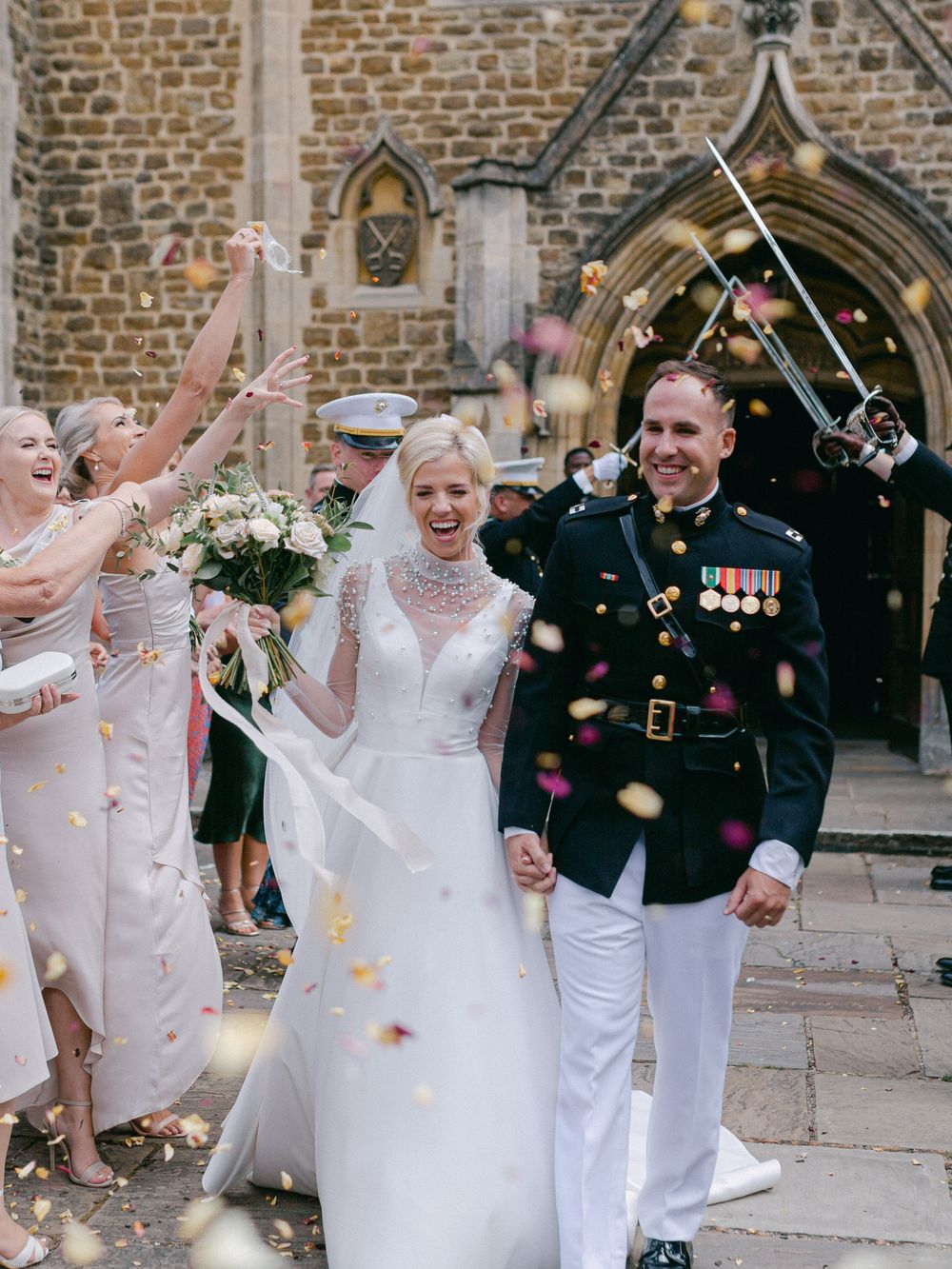 A military wedding celebration outside a stone church with confetti being thrown as the newlyweds exit.