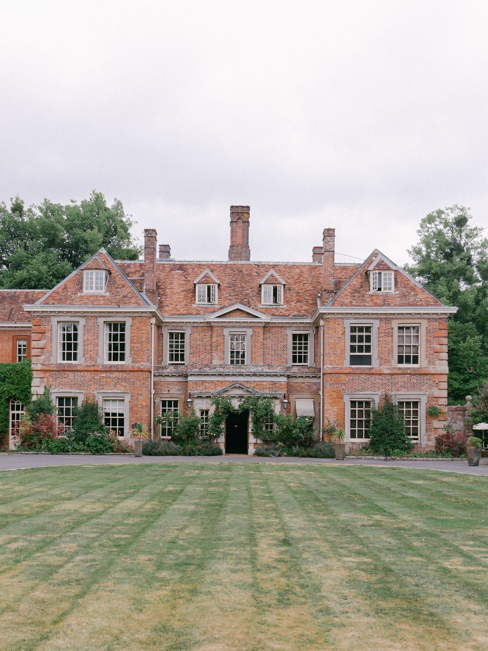 Grand brick Georgian manor house with dormer windows and manicured lawn.