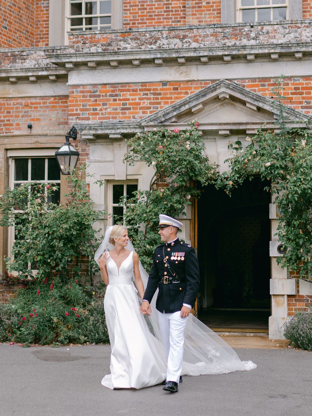 Newlyweds walk hand in hand outside historic brick building with ivy-covered walls.