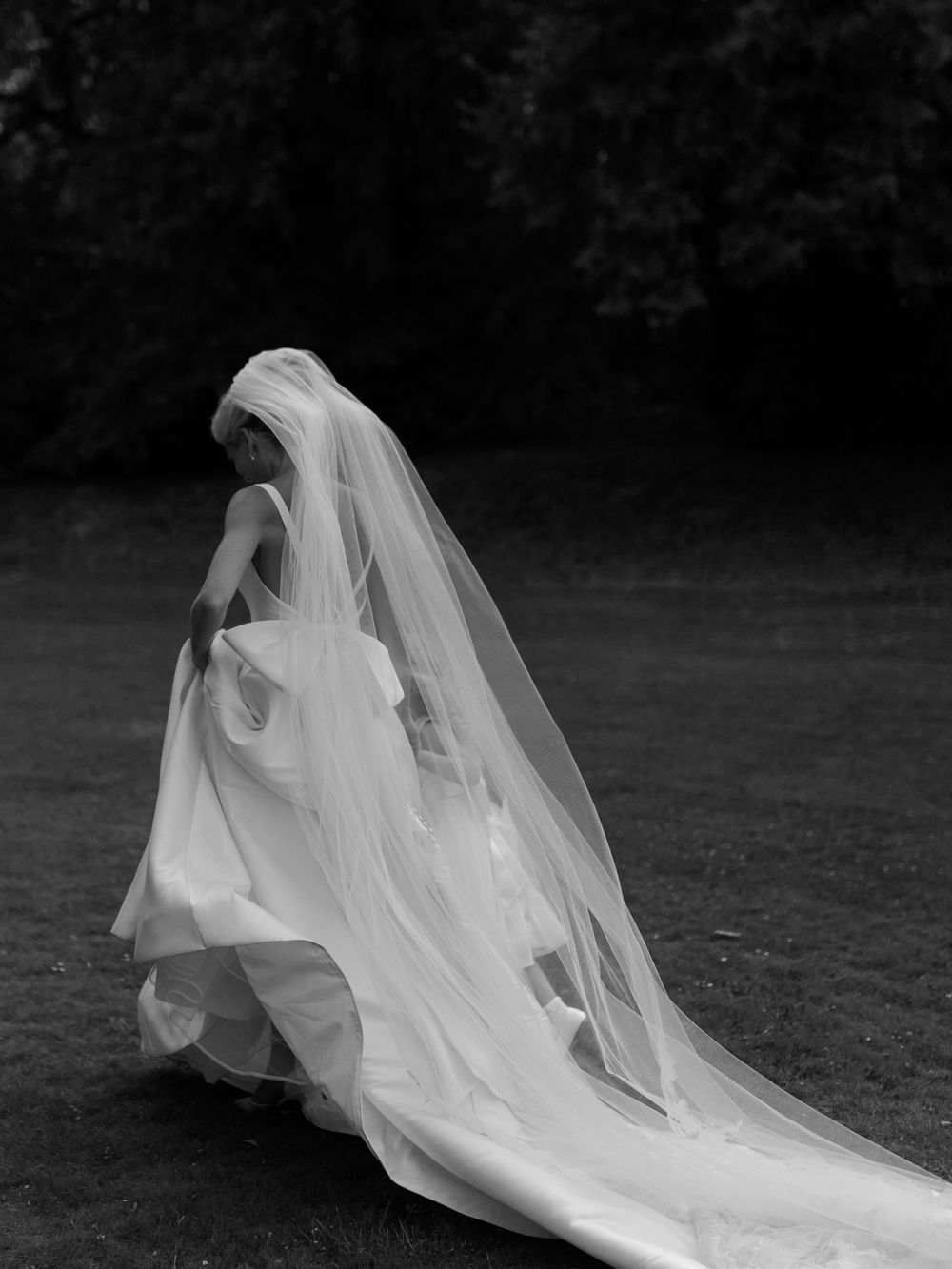 A long flowing white wedding veil billows dramatically in the wind against a dark background.