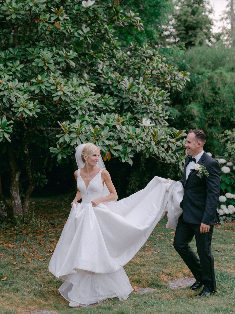 A flowing white wedding dress twirls gracefully in a garden setting with lush greenery in the background.