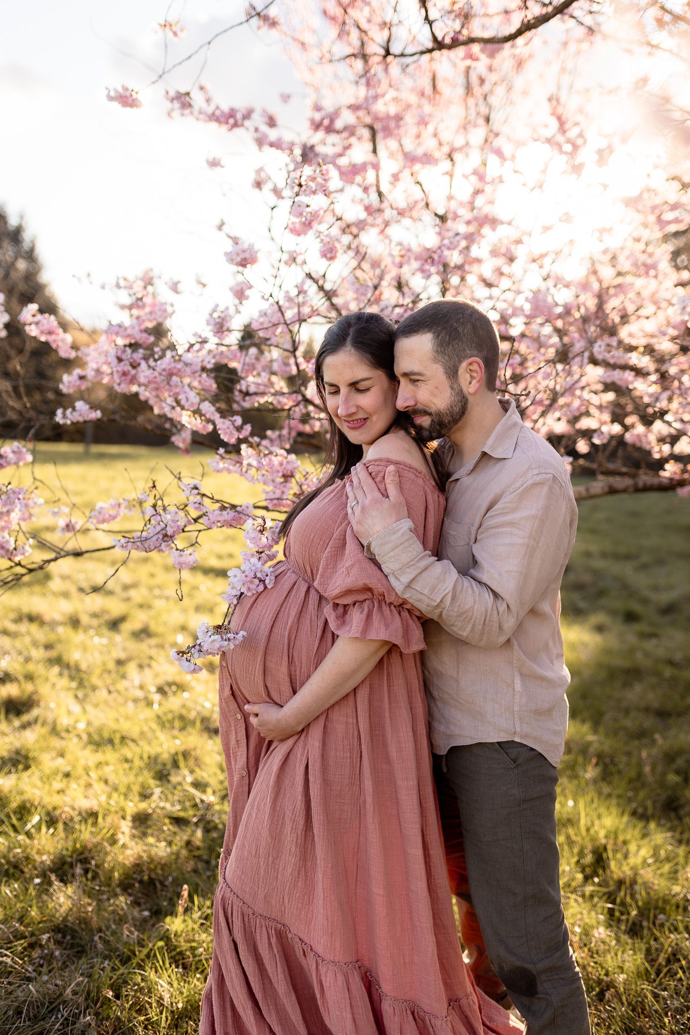 Couple attendant un bébé sous les cerisiers en fleurs à Versailles au coucher du soleil