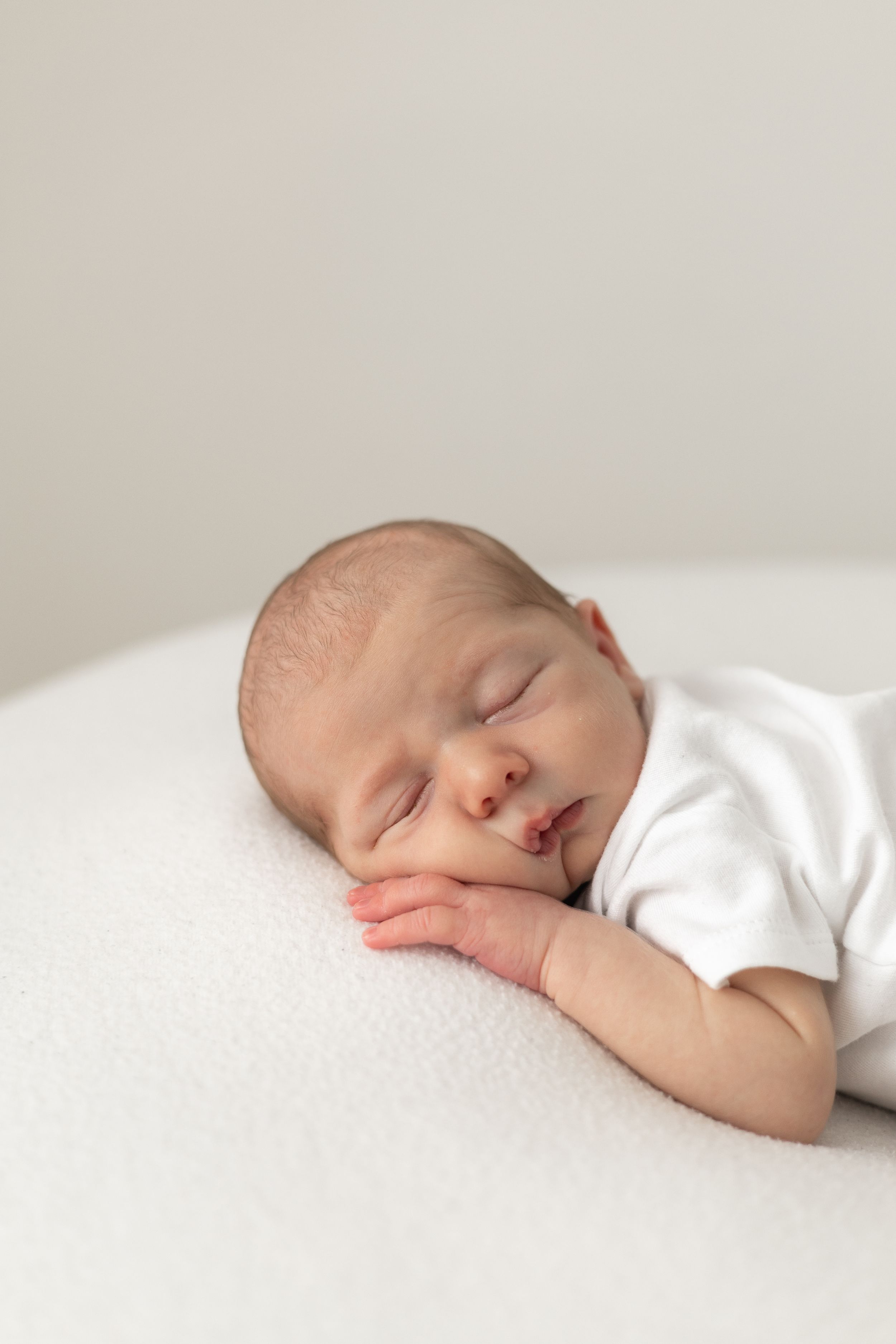 Relaxed newborn photoshoot Nottingham baby curled up studio session peaceful newborn baby sleeping on white blanket