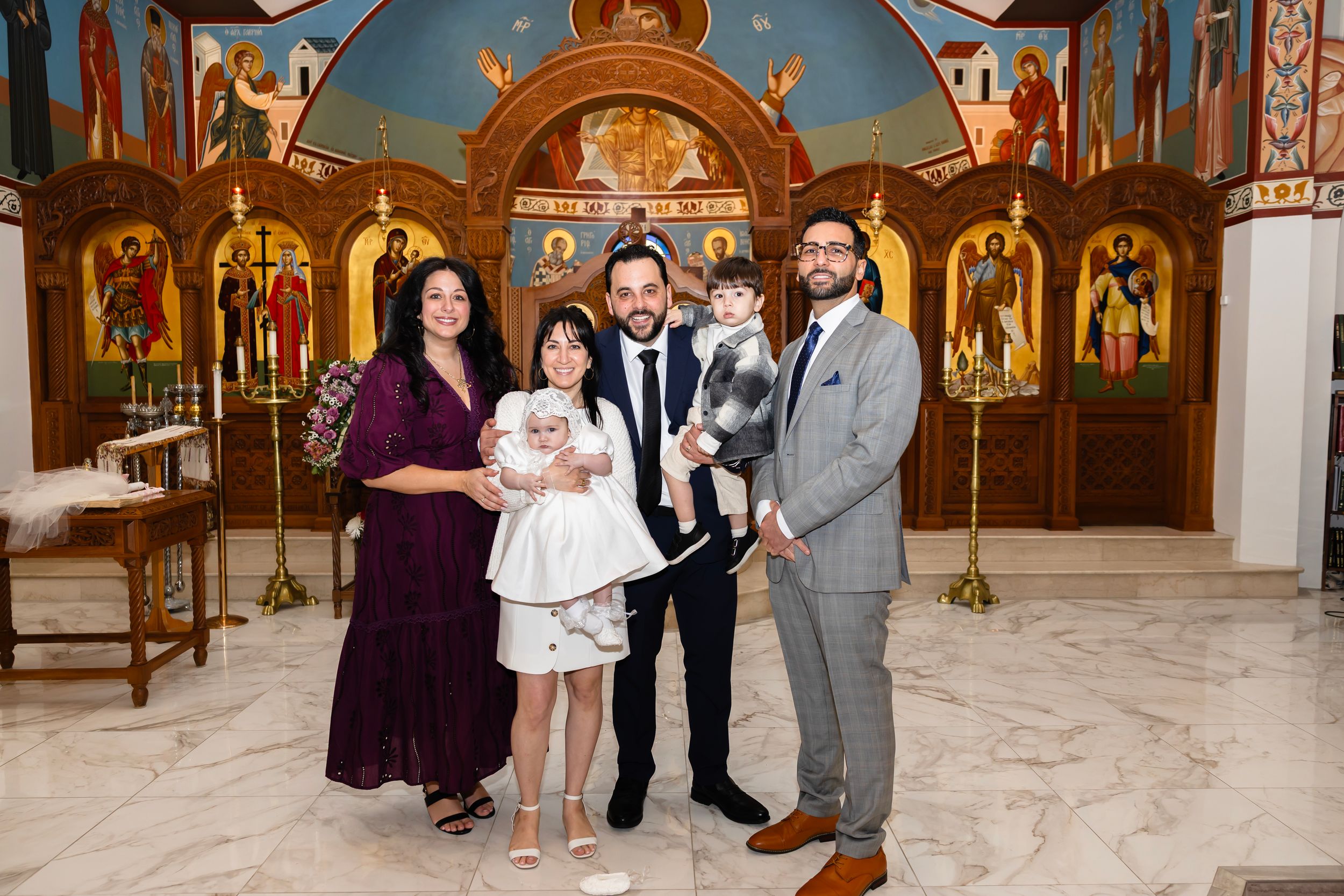 Family posing together inside an Orthodox church with ornate iconostasis during a baptism ceremony.