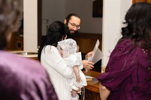 Parents holding a baby in a white christening gown during a baptism ceremony inside a church.