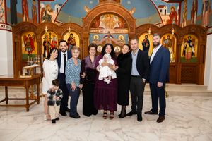 Family group photo at a Greek Orthodox church baptism ceremony with ornate gold iconostasis backdrop.