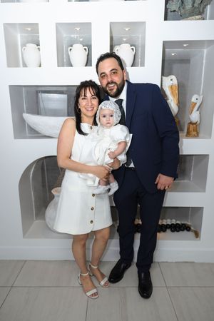 Family portrait with parents holding baptized baby in white christening outfit at reception venue.